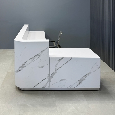 90-inch Nola L-Shape Custom Reception Desk with the l-panel on the right side when facing front with a 36-inch low extension. The main desk is covered in calcutta stone PVC, and the toe-kick in brushed aluminum. 