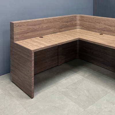 72-inch Nola L-Shape Custom Reception Desk with the l-panel on the right side when facing front with a 36-inch low extension. The main desk is covered in hazel walnut matte laminate and the toe-kick in brushed aluminum.