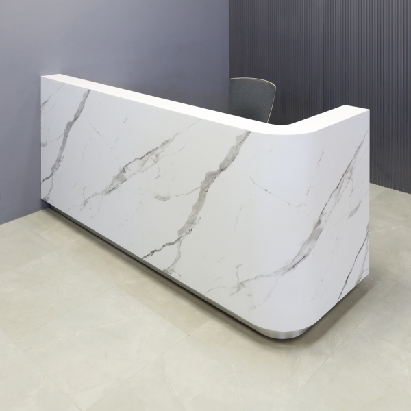 90-inch Nola L-Shape Custom Reception Desk with the l-panel on the right side. The main desk is covered in calcutta stone PVC, and the toe-kick in brushed aluminum.